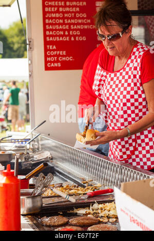 Lauch & Bezirk SHOW, Lauch, STAFFORDSHIRE, ENGLAND A Frau trägt rot karierte Schürze dient einen Hot Dog von einem Burger-stand Stockfoto