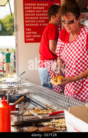 Lauch & Bezirk SHOW, Lauch, STAFFORDSHIRE, ENGLAND A Frau trägt rot karierte Schürze dient einen Hot Dog von einem Burger-stand Stockfoto