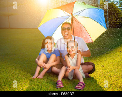 Vater und Töchter sitzen auf einer Wiese mit bunten Regenschirm Stockfoto