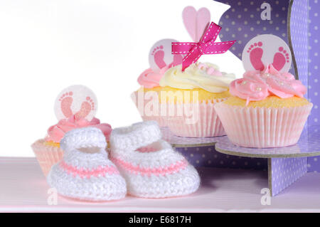 Rosa Thema Baby Mädchen Cupcakes und Booties, Großaufnahme auf lila Tupfen Cupcake Ständer vor weißem Hintergrund Stockfoto