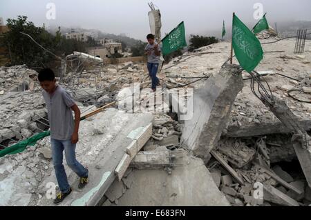 Hebron, Westjordanland, Palästinensische Gebiete. 18. August 2014. Palästinensischen Jungen halten Nationalflaggen, wie sie auf den Trümmern der ein Hossam Al-Kawasmi des Hauses zerstört durch die israelische Armee, in der West Bank von Hebron am 18. August 2014 stehen. Der israelischen Armee zerstört, die Häuser der beiden Verdächtigen im Junis Entführung und Ermordung von drei israelischen Jugendlichen späten Montagabend, während zusätzlich die Residenz eines dritten Abschottung vermute Credit: Mamoun Wazwaz/APA Bilder/ZUMA Draht/Alamy Live News Stockfoto