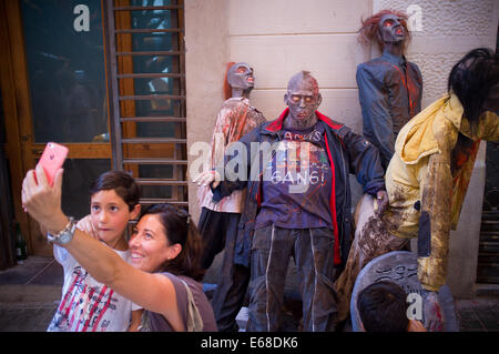 Barcelona, Spanien. 18. August 2014. Menschen nehmen ein Selbstporträt in der Nähe von Zombies in Gracia Viertel von Barcelona. Progres Street wurde im Stadtteil Gracia von Barcelona, wie ein Zombie-Welt durch das traditionelle Sommerfest Festes de Gràcia, die beliebteste in der katalanischen Stadt angepasst. Bildnachweis: Jordi Boixareu/Alamy Live-Nachrichten Stockfoto