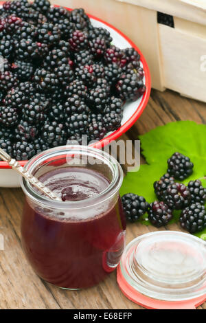 Erntefrisch Wald, die Brombeeren in einer Schüssel mit einem Glas Brombeere auf einem rustikalen Holztisch im Garten Marmelade Stockfoto