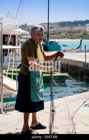 Frau Sortting Fischernetze am Kai, Marsaxlokk, Malta. Stockfoto