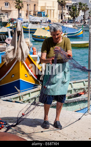 Frau Sortierung Fischernetze am Kai, Marsaxlokk, Malta. Stockfoto