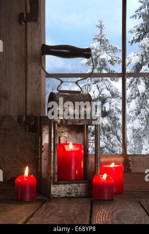 Alte hölzerne Fensterbank dekoriert mit vier roten Weihnachtskerzen. Blick auf den verschneiten Bäumen in den Bergen. Stockfoto