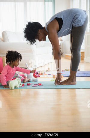 Mutter, Dehnung, wie Tochter auf Yoga-Matte spielt Stockfoto