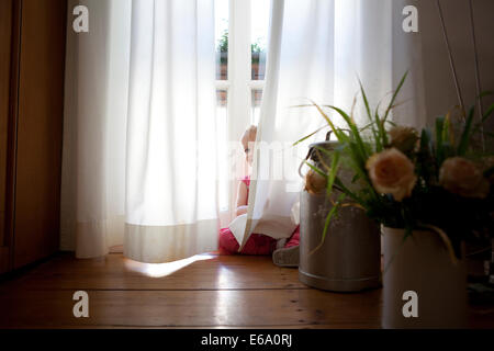 Junges Mädchen spielen und peering hinter undurchsichtigen weißen Vorhängen. Stockfoto