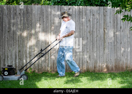 Ein senior Mann trägt einen Hut mäht seinen Rasen in gefleckten Sonne und Schatten in Oklahoma, USA Stockfoto