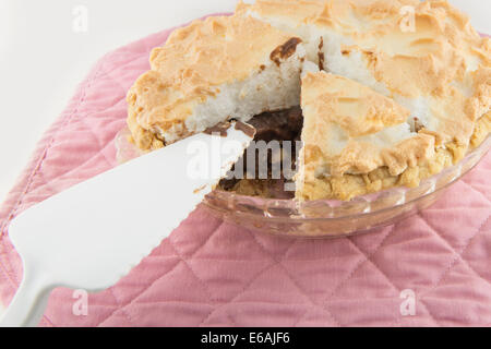 Eine hausgemachte Schokolade Meringue Pie mit einem Stück gegangen, dargestellt mit einer Portion utensil auf einem rosa Mat. Nahaufnahme. USA. Stockfoto