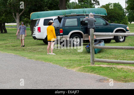 Ein Mann sichert ein Kanu auf sein Fahrzeug an einem Oklahoma See während zwei Familienmitglieder sind in der Nähe. Oklahoma, USA. Stockfoto