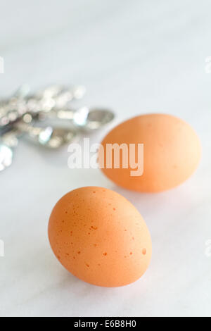 Ein Foto von zwei braune Eier auf einem Marmor Kuchen mit Messlöffel in der Hintergrund verschwommen. Stockfoto