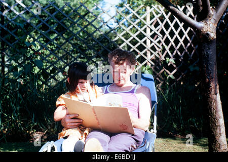 Vater liest eine Geschichte seiner jungen Tochter im Garten an einem heißen Sommertag im Jahr 1976 England uk Stockfoto