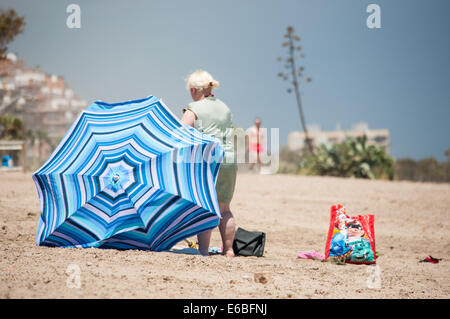 Eine ältere Frau am Strand mit ihrem Schirm Stockfoto
