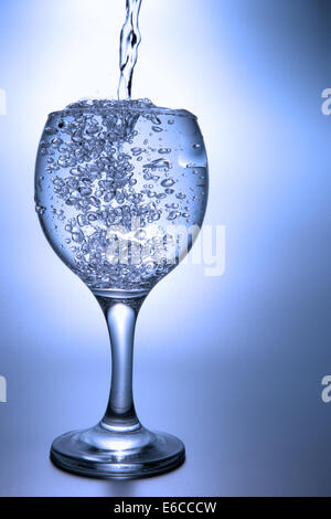 Klarer Flüssigkeit auf blauem Hintergrund in footed Glas gießen. Stockfoto