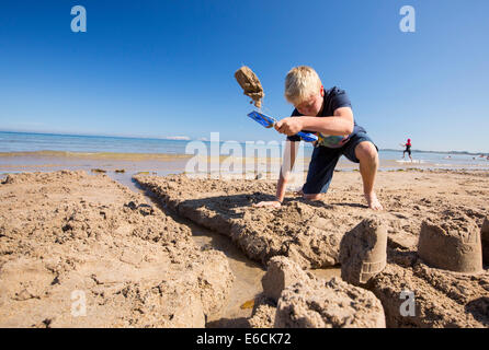 Ein Junge, bauen eine Sandburg am Strand von Bamburgh, Northumberland, UK. Stockfoto