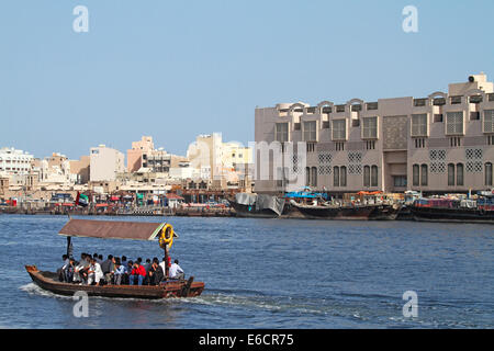 Holzboot, traditionellen Abra als kleine öffentliche Fähre mit Passagieren am Dubai Creek, mit Wasser Gebäude & Dhaus in Stadt Dubai Stockfoto