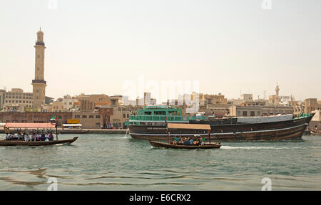 Boote aus Holz, einschließlich der traditionellen Dhau und kleine Fähren (Abras) auf ruhigen Gewässern des Dubai Creek mit Gebäuden und Moschee in Dubai im Hintergrund Stockfoto