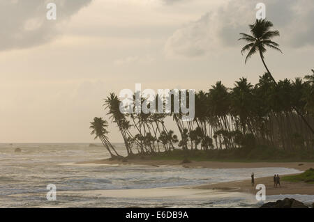 Männer gehen auf einen Strand vor Palmen gesäumten Landzunge, mit Spray von stürmischer See bei Sonnenuntergang, Galle, Sri Lanka Stockfoto
