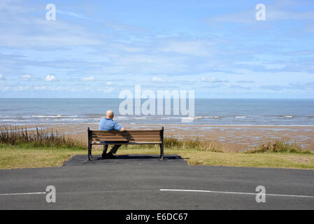 Einsame ältere Mann sitzt auf Holzbank mit Blick aufs Meer in Blackpool, Lancashire. Stockfoto