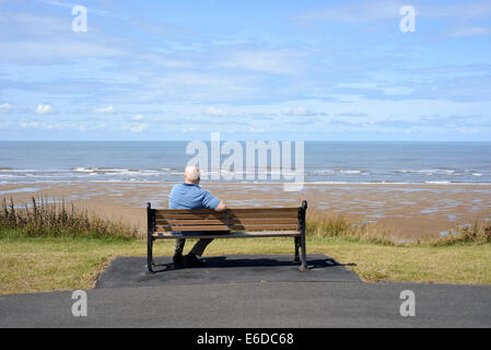 Einsame ältere Mann sitzt auf Holzbank mit Blick aufs Meer in Blackpool, Lancashire. Stockfoto