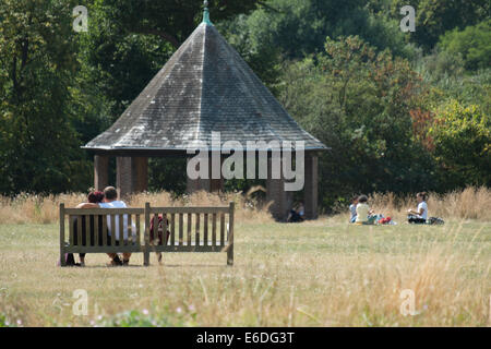 Paar auf einer Bank mit Familie im Hintergrund an einem warmen Sommertag im Londoner Hyde Park Stockfoto