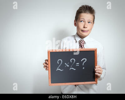 Der nette lustige Schuljunge Teenager in ein weißes Hemd denken über die Entscheidung der Aufgabe auf die schwarze Tafel Stockfoto