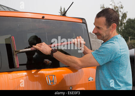 Mann Waschen Fahrzeug Windschutzscheibe an Tankstelle Stockfoto