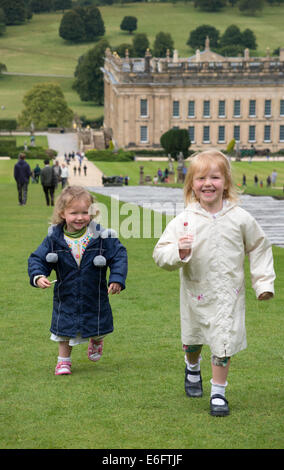 Junge Mädchen, Schwestern im Alter von drei und fünf Jahren laufen und spielen im Garten von Chatsworth House Nr Bakewell in Derbyshire. UK. Mädchen sind Model Released. Stockfoto