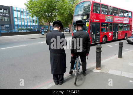 Junge orthodoxe jüdische Männer mit Fahrrad warten Doppeldecker roten Bus Verkehr auf Straße überqueren in Stamford Hill im Norden von London N16 UK KATHY DEWITT Stockfoto