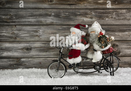 Lustiges aus Holz Weihnachten Hintergrund mit zwei Santa Claus auf einem Fahrrad, das Weihnachten einkaufen. Auch witzige Konzept für die Teamarbeit. Stockfoto