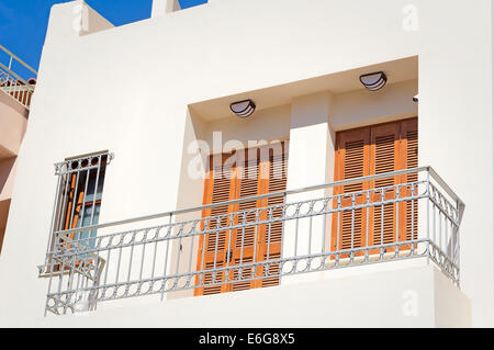 Fragment einer Fassade des alten Hauses an der Küste der Insel Kreta mit einem Balkon und alten hölzernen Jalousien vor der Sonne. Stockfoto