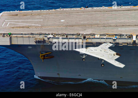 Die US Navy X-47 b, die autonomen stealth unbemannten das Flugdeck des Flugzeugträgers USS Theodore Roosevelt während Tests demonstriert die Fähigkeit vorbeifliegt, sicher und nahtlos mit bemannten Luftfahrzeugen 17. August 2014 in den Atlantischen Ozean zu betreiben. Stockfoto