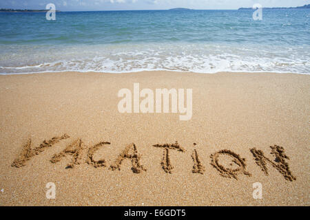 "Urlaub" in den Sand am Strand mit blauen Wellen im Hintergrund geschrieben Stockfoto