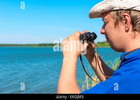 hübscher junger Mann mit dem Fernglas am See Stockfoto