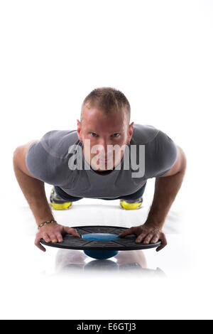 Junge blonde muskulöser Mann Ausübung auf dem Boden mit Balance Disc Board isoliert auf weiss Stockfoto