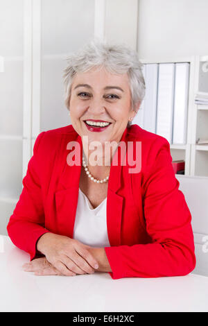 Attraktive ältere senior Geschäftsfrau am Schreibtisch sitzen. Stockfoto