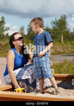 Mutter und sechs Jahre alten jungen Kind spielen zusammen im Sandkasten Stockfoto