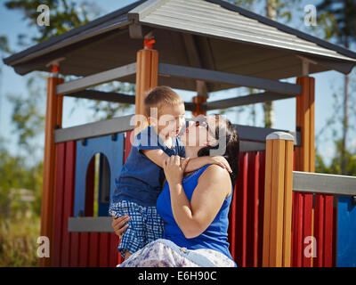 Sechs Jahre alter Junge Umarmung seiner Mutter, Spielplatz im Hintergrund Stockfoto