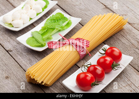 Tomaten, Mozzarella, Nudeln und grüner Salat Blätter auf Holztisch Hintergrund Stockfoto