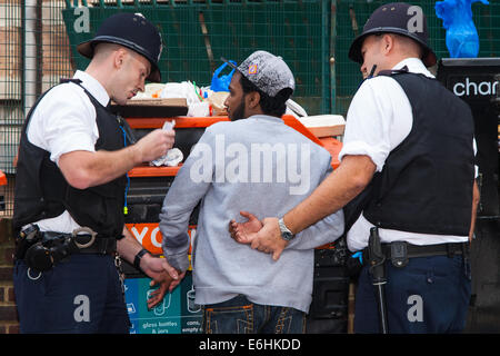 London, UK. 24. August 2014. Polizei einen jungen Mann zu suchen, als Tausende von Londonern aller Rassen und Kulturen besuchen Notting Hill Carnival 'Familienfreundlich' Tag vor dem wichtigsten Karneval am August Bank Holiday Montag. Bildnachweis: Paul Davey/Alamy Live-Nachrichten Stockfoto