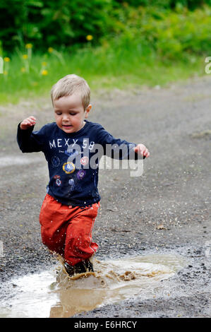 Ein kleiner Junge durchnässt läuft durch eine Pfütze Stockfoto