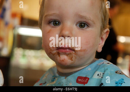 Ein zweijähriges Kind mit Schokoladensauce über das ganze Gesicht Stockfoto