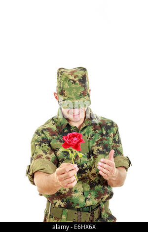 Offizier in der Armee hält Blume Lächeln schüchtern mit Kopf neigte, Krieg romantisches Konzept Stockfoto