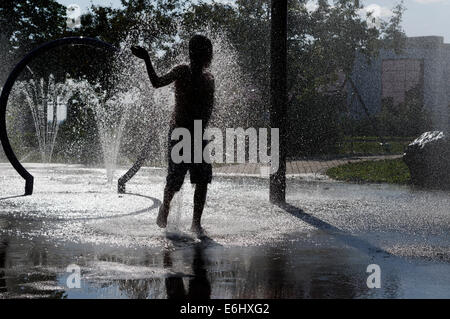 Ein kleiner Junge spielt im Wasserbrunnen an einem heißen Sommertag Stockfoto