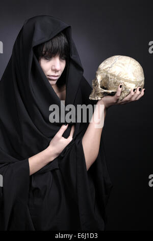 Frau mit einem menschlichen Schädel. Mit schwarzem Tuch bedeckt. Stockfoto