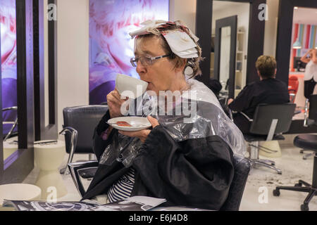 ÄLTERE FRAU IM FRISEURSALON MIT HIGHLIGHTS INS HAAR BEIM TRINKEN KAFFEE. ENGLAND-UK Stockfoto