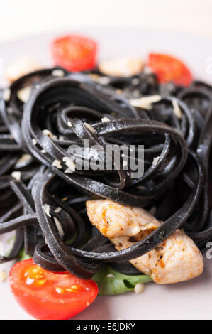 Frische schwarze Tagliolini Nudeln mit Huhn in Kräutern auf Rucola und Tomaten Stockfoto