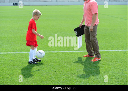 Junge 9 10 11 spielen Futbol Fußball auf grasbewachsenen Pitch Bereich Aufwärmen mit Trainer üben Stockfoto