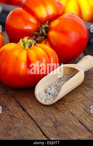 Reife Beefsteak Tomaten und Salz in Spice Schaufel auf einem alten rustikalen Schneidebrett im Landhausstil Stockfoto